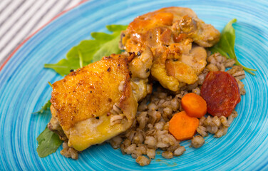 Delicious barley porridge with roasted chicken thighs and vegetables decorated fresh arugula on ceramic plate..
