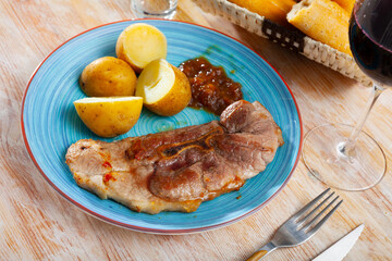 Appetizing fried pork on bone served with boiled potatoes in their skins and caramelized onions on blue plate