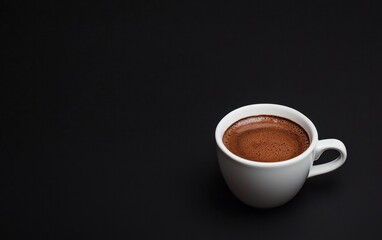 Fototapeta premium Close-up view of a small white cup filled with dark brown espresso on a black background. The crema is visible on top of the coffee