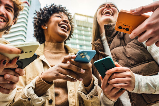 Happy young people using smart mobile phone device outside - Technology concept with guys and girls watching cellphone in city street