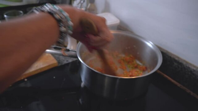 Chef mixes sofrito in a pot on an induction stove