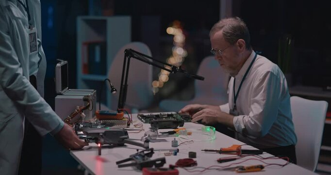 Bearded adult caucasian engineer sitting at desk in office soldering microship or circuit board engineering looking for camera. Portrait of professional electronic technician.