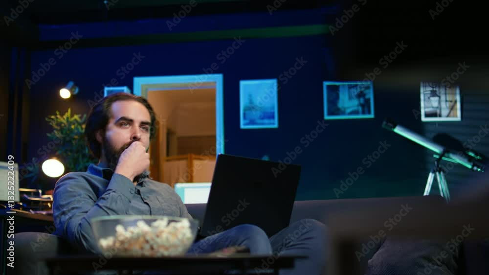 Aufkleber man working on laptop lounged on neon lit apartment couch while picking tv channel to watch as distr
