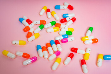 Scattered colorful capsules with happy faces on isolated pink background. Medication in healthcare. Vitamins, supplements, health, happiness and pills concept. Top view 