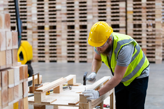 Worker constructs wooden furniture in a warehouse during daylight hours