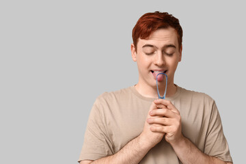 Young man with tongue scraper on grey background
