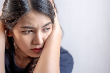 Fototapeta premium A young woman has a worried expression, holding her head, showing stress and anxiety, reflecting the state of a person suffering from depression.