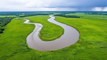 Naklejka premium Serpentine River Flowing Through Lush Green Fields Under Cloudy Sky