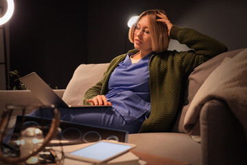 Female nurse with laptop on sofa working evening shift in clinic