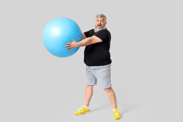 Overweight shocked mature man with fitness ball on grey background. Weight loss concept