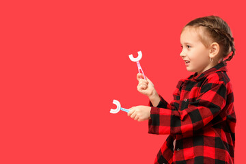 Happy little girl in checkered pajamas with toothbrushes on red background