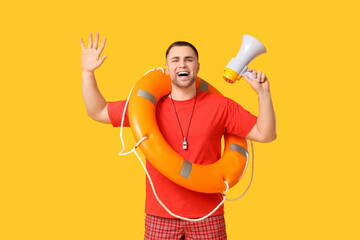 Happy young lifeguard with lifebuoy and megaphone raising hands on yellow background
