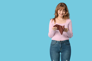 Beautiful young woman holding brown wallet on blue background