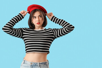 Portrait of fashionable young woman in beret on blue background