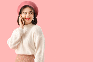 Portrait of fashionable young woman in beret talking by phone on pink background