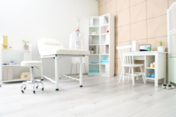 Blurred view of medical office with couch, shelf units and doctor's workplace
