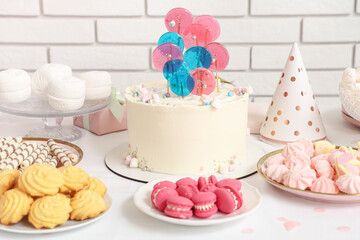 Table with cake and sweets for birthday party against white brick wall