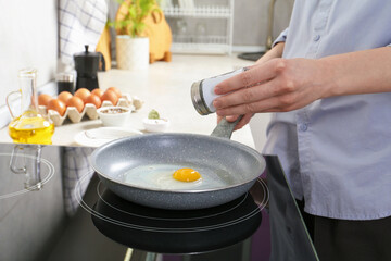 Woman adding salt into frying pan while cooking eggs on cooktop in kitchen, closeup