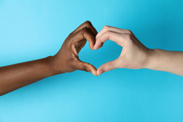 Stop racism. People of different skin colors making heart with hands on light blue background, closeup