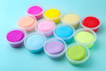 Different colorful modeling clay in plastic jars on light blue background