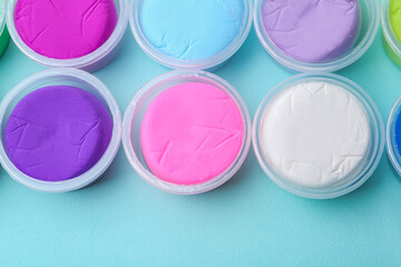 Different colorful modeling clay in plastic jars on light blue background, flat lay