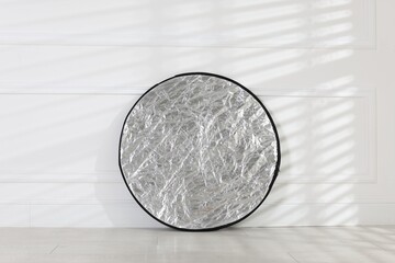 Professional reflector on floor near white wall. Photo studio equipment