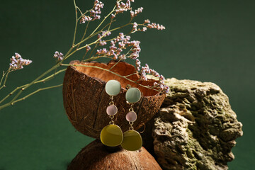 Coconut shell, dried flower and stone with beautiful earrings on green background. Closeup