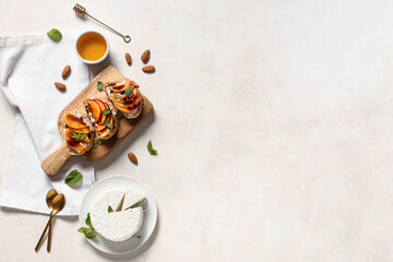 Wooden board of peach bruschetta with ricotta, mint, almond nuts and bowl of honey on white...