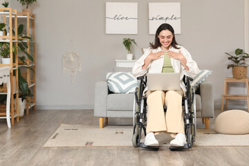 Young woman in wheelchair with laptop video chatting at home