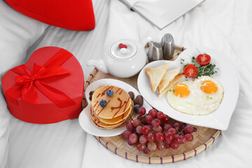 Tasty breakfast with gift for Valentine's Day on bed, closeup