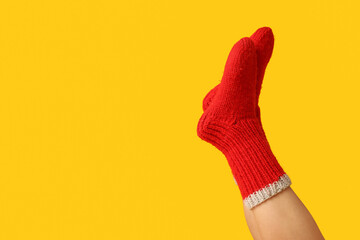 Legs of young woman in red knitted socks on yellow background