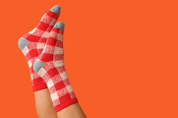 Legs of young woman in warm checkered socks on orange background