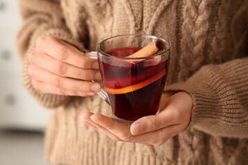 Woman holding glass cup of hot mulled wine at home, closeup
