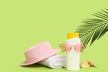 Composition with bottle of sunscreen cream, hat, towel and sunglasses on green background