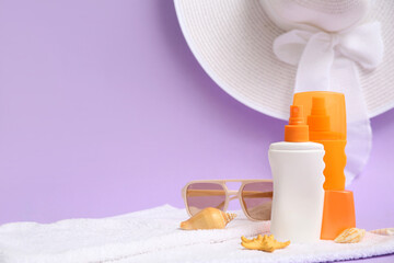 Sunglasses, towel, hat and bottles of sunscreen cream on lilac background