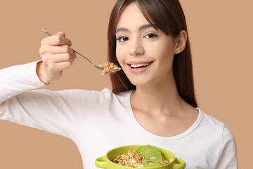 Young woman eating tasty granola with kiwi on beige background