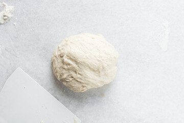 Overhead view of high hydration dough being shaped on a white granite countertop, top view of homemade bread dough on white countertop, process of making artisan bread