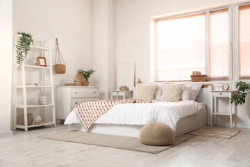Big comfortable bed and bedside tables near window in interior of light bedroom