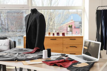 Blank laptop with men's clothes on tailor's table in atelier