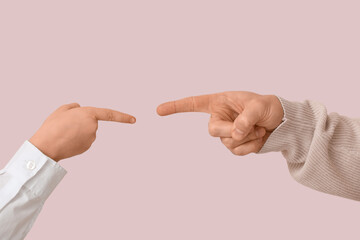 Hands of father and his son pointing at each other while squabbling on pink background, closeup