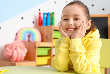 Cute little girl sitting at table in room