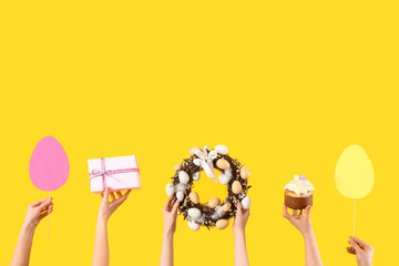 Female hands with Easter cake, paper eggs and gift on yellow background