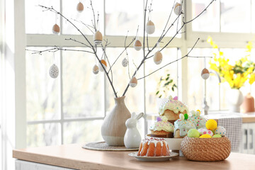 Vase with tree branches, Easter cakes and eggs on table in kitchen