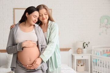 Young pregnant lesbian couple hugging in bedroom