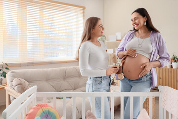 Young pregnant lesbian couple with toy near baby crib at home