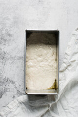 Overhead view of focaccia dough in a loaf baking tin, dough rising in a loaf pan, process of making focaccia