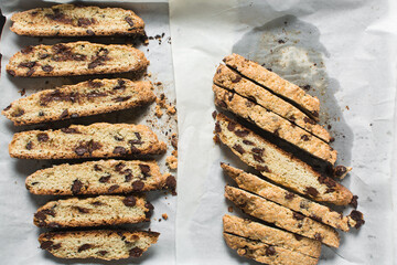 Overhead view of chocolate chip biscotti on white parchment lined tray, top view of chocolate chip cantucci cookies on a white board, flatlay of slices of biscotti cookies or twice baked cookies