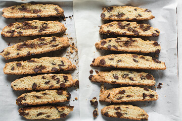 Overhead view of chocolate chip biscotti on white parchment lined tray, top view of chocolate chip cantucci cookies on a white board, flatlay of slices of biscotti cookies or twice baked cookies