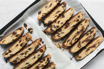 Overhead view of chocolate chip biscotti on white parchment lined tray, top view of chocolate chip cantucci cookies on a white board, flatlay of slices of biscotti cookies or twice baked cookies