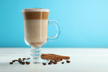 Tasty latte macchiato in glass cup, coffee beans and cinnamon on white wooden table, closeup. Space...